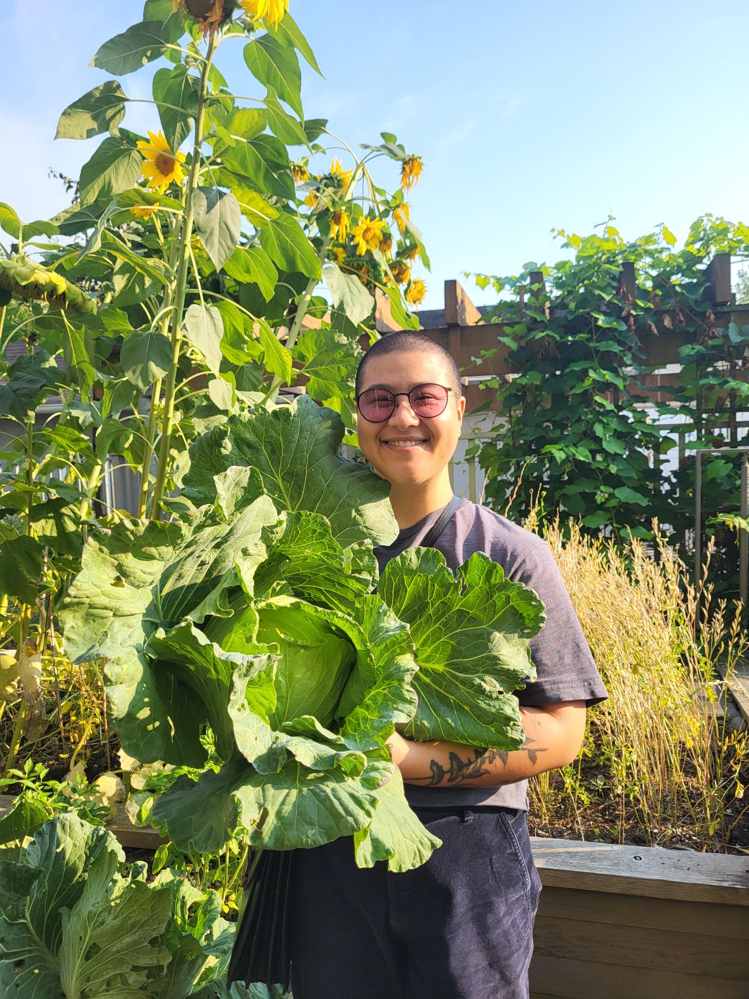 Maria standing in an outdoor garden. They are holding a large cabbage.