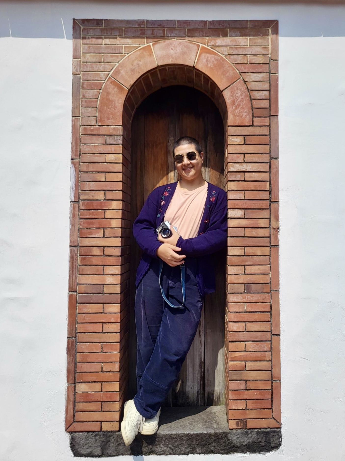 Maria standing in an architectural arch feature. The arch is red brick and the rest of the wall is white plaster.